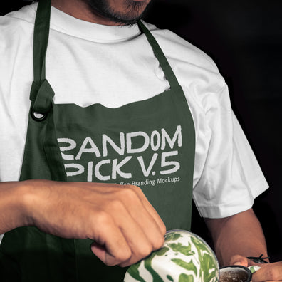 Close-up of a barista in a dark green apron mockup holding a latte art cup mockup with matcha green swirl, dark moody background, perfect for coffee brand identity mockup