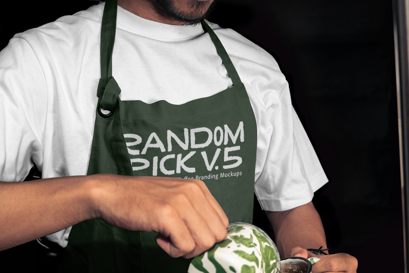 Close-up of a barista in a dark green apron mockup holding a latte art cup mockup with matcha green swirl, dark moody background, perfect for coffee brand identity mockup