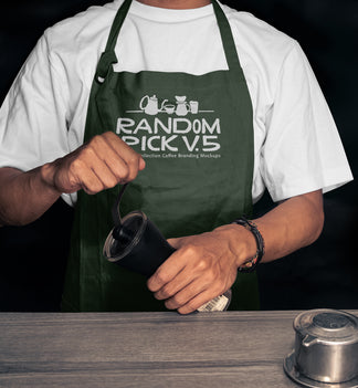 Realistic dark green barista apron mockup worn by a man holding a coffee grinder on a moody dark background with coffee props on a wooden table