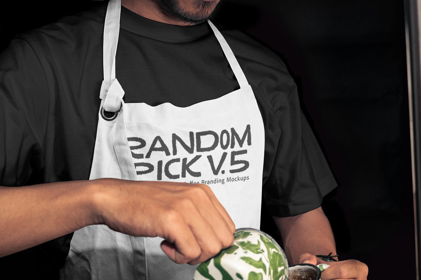 Close-up of a barista in a white apron mockup holding a latte art cup mockup with matcha green swirl, dark moody background, perfect for coffee brand identity mockup