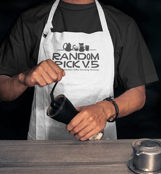 Realistic white barista apron mockup worn by a man holding a coffee grinder on a moody dark background with coffee props on a wooden table