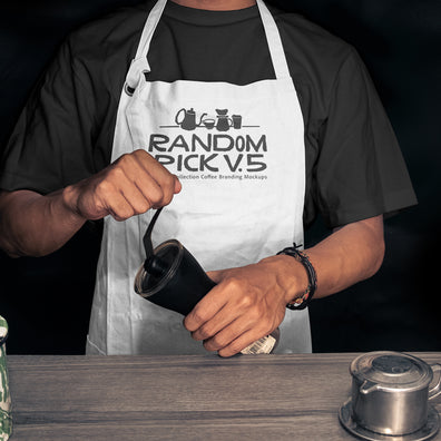 Realistic white barista apron mockup worn by a man holding a coffee grinder on a moody dark background with coffee props on a wooden table