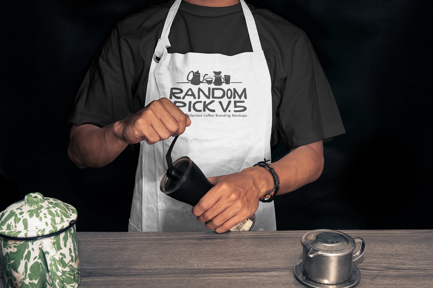 Realistic white barista apron mockup worn by a man holding a coffee grinder on a moody dark background with coffee props on a wooden table