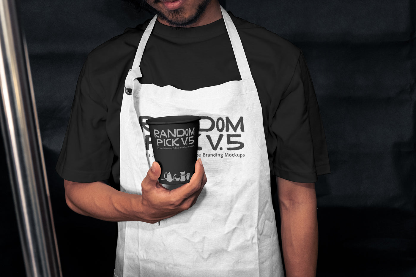 Barista wearing a white apron holding a branded paper coffee cup in a moody dark cafe setting, showing both apron and cup branding mockup
