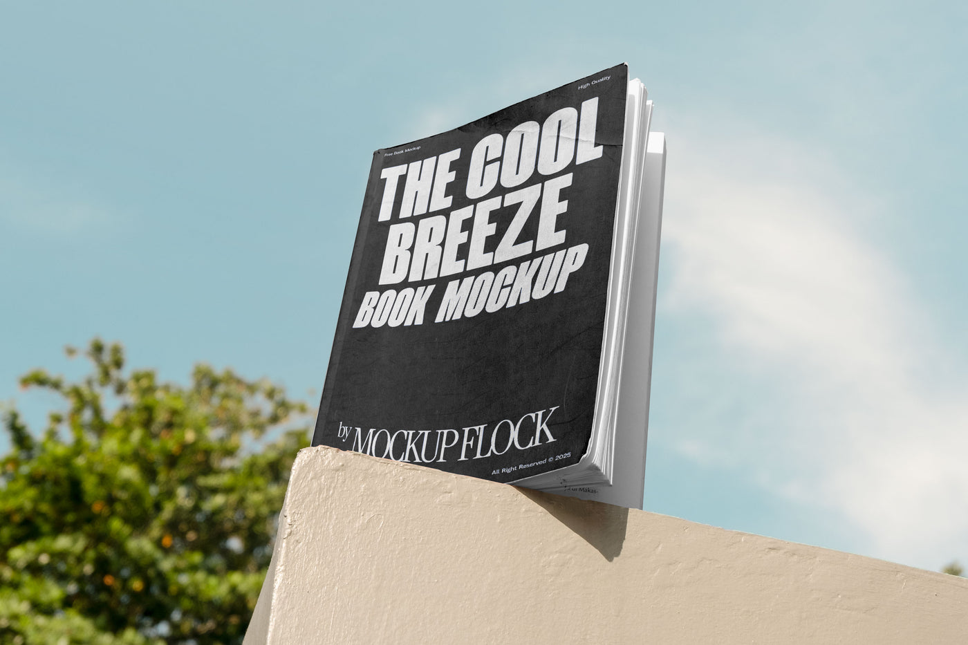 A black book with white text reading THE COOL BREEZE BOOK MOCKUP BY MOCKUP FLOCK is lying on a fence, displayed in a natural outdoor setting.
