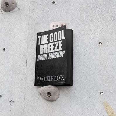 A black book with white text reading THE COOL BREEZE BOOK MOCKUP BY MOCKUP FLOCK is lying on a rock climbing wall. Design by Mockup Flock