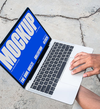 A person is holding an Macbook Device that says "MOCKUP THE COOL BREEZE COLLECTION @2025" in bold white text. Design by Mockup Flock