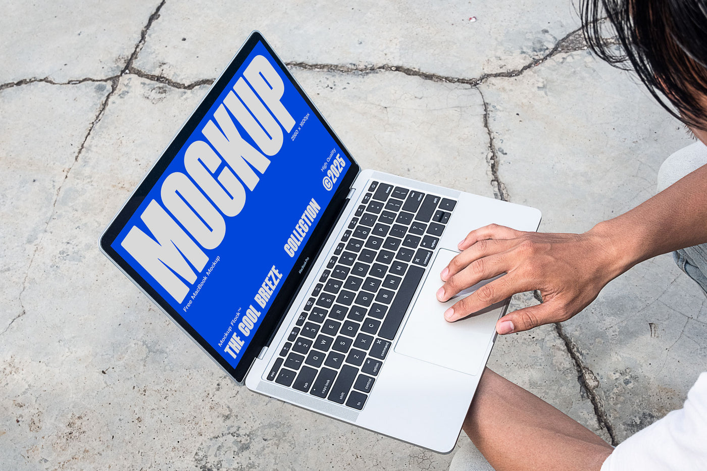 A person is holding an Macbook Device that says "MOCKUP THE COOL BREEZE COLLECTION @2025" in bold white text. Design by Mockup Flock