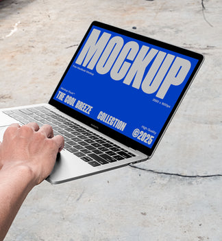 A person is holding an Macbook Device that says "MOCKUP THE COOL BREEZE COLLECTION @2025" in bold white text. Design by Mockup Flock