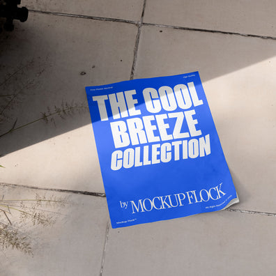 A blue Poster with white text reading THE COOL BREEZE COLLECTION BY MOCKUP FLOCK is lying on a floor, displayed in a natural outdoor setting.