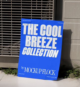 A blue Poster with white text reading THE COOL BREEZE COLLECTION BY MOCKUP FLOCK is lying on the grassy floor, attached to the outdoor air conditioner.