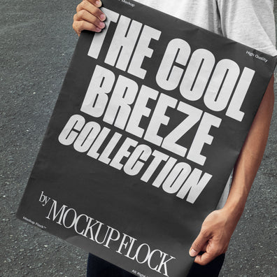 A person holds a poster that reads "THE COOL BREEZE COLLECTION BY MOCKUP FLOCK" in bold text, standing on black asphalt.
