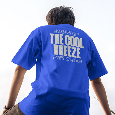 A person wearing a t-shirt that says "MOCKUP FLOCK THE COOL BREEZE T-SHIRT: 31,5X45CM" in bold text, on a blue sky background.