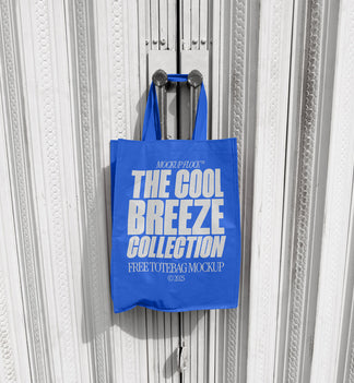 A blue tote bag with white text that reads "THE COOL BREEZE COLLECTION FREE TOTE BAG MOCKUP" hanging on a door handle.