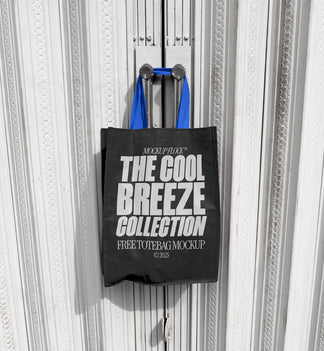 A black tote bag with white text that reads "THE COOL BREEZE COLLECTION FREE TOTE BAG MOCKUP" hanging on a door handle.