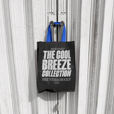 A black tote bag with white text that reads "THE COOL BREEZE COLLECTION FREE TOTE BAG MOCKUP" hanging on a door handle.