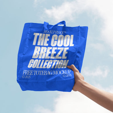 A person holds a tote bag that says "MOCKUP FLOCK THE COOL BREEZE COLLECTION FREE TOTE BAG MOCKUP" in bold text, on a blue sky background.