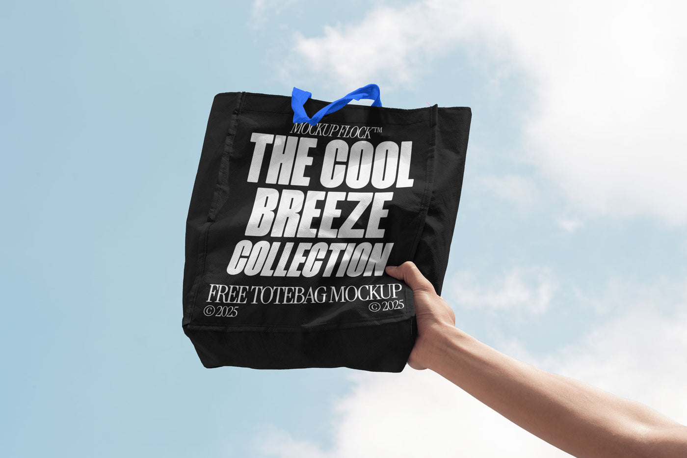 A person holds a tote bag that says "MOCKUP FLOCK THE COOL BREEZE COLLECTION FREE TOTE BAG MOCKUP" in bold text, on a blue sky background.