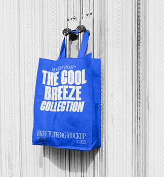 A blue tote bag with white text that reads "THE COOL BREEZE COLLECTION FREE TOTE BAG MOCKUP" hanging on a door handle.