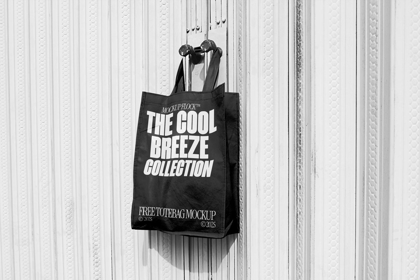 A black tote bag with white text that reads "THE COOL BREEZE COLLECTION FREE TOTE BAG MOCKUP" hanging on a door handle.