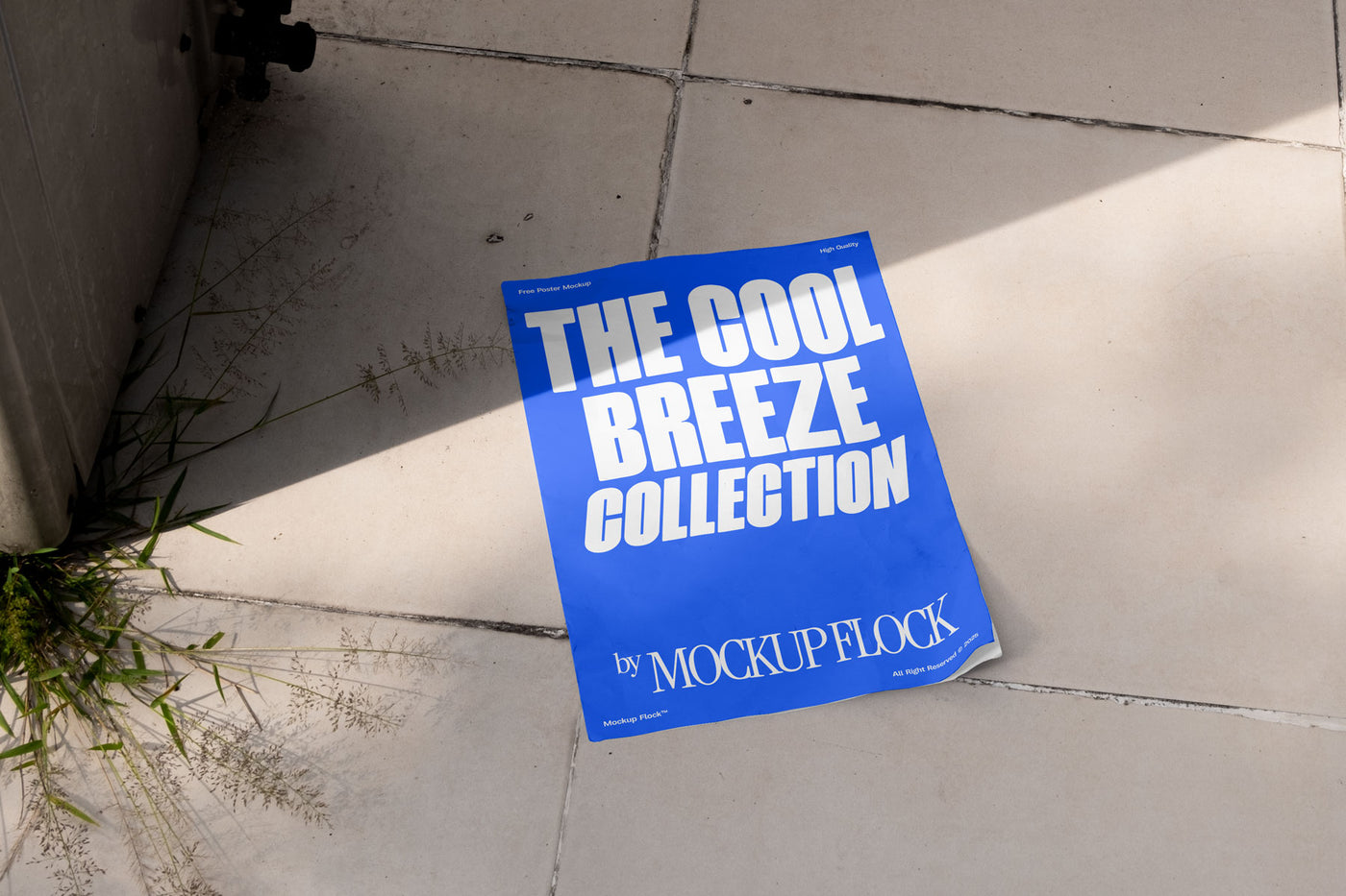 A blue Poster with white text reading THE COOL BREEZE COLLECTION BY MOCKUP FLOCK is lying on a floor, displayed in a natural outdoor setting.