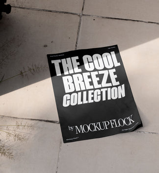 A black Poster with white text reading THE COOL BREEZE COLLECTION BY MOCKUP FLOCK is lying on a floor, displayed in a natural outdoor setting.