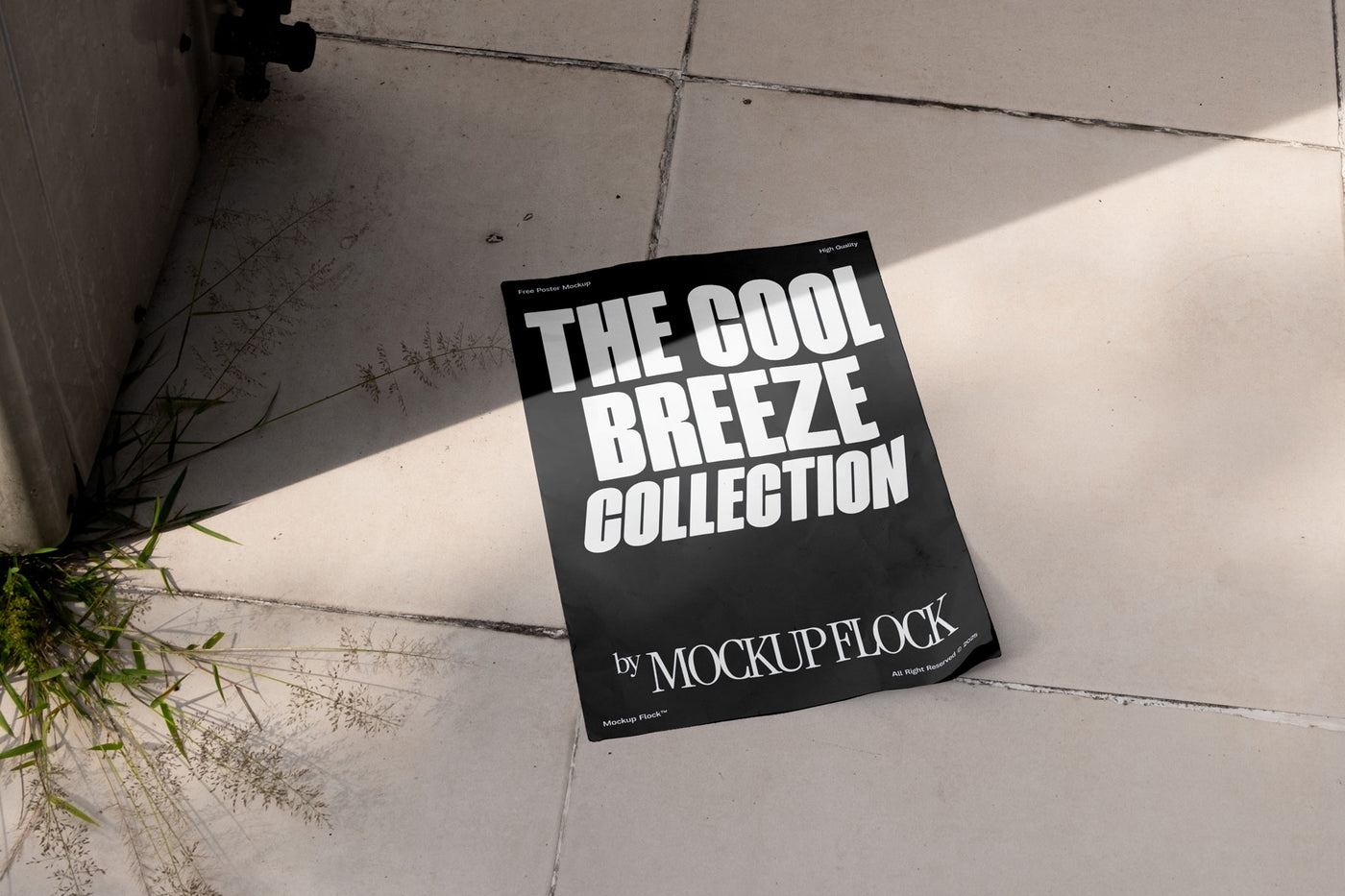 A black Poster with white text reading THE COOL BREEZE COLLECTION BY MOCKUP FLOCK is lying on a floor, displayed in a natural outdoor setting.