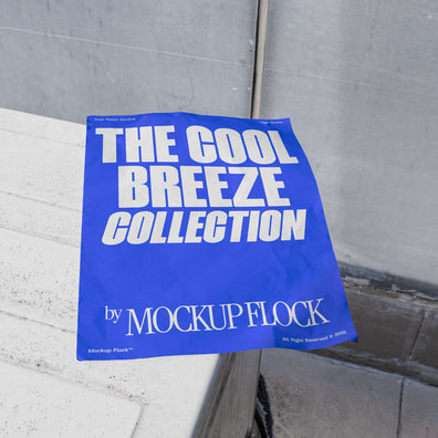 A blue Poster with white text reading THE COOL BREEZE COLLECTION BY MOCKUP FLOCK is lying on a box white, displayed in a outdoor setting.