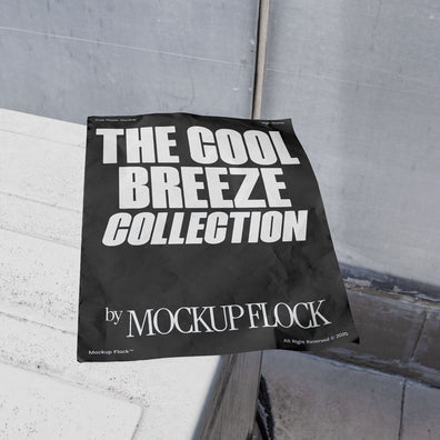 A black Poster with white text reading THE COOL BREEZE COLLECTION BY MOCKUP FLOCK is lying on a box white, displayed in a outdoor setting.