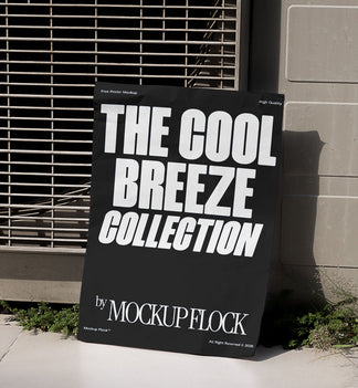 A black Poster with white text reading THE COOL BREEZE COLLECTION BY MOCKUP FLOCK is lying on the grassy floor, attached to the outdoor air conditioner.