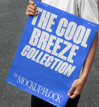 A person holds a poster that reads "THE COOL BREEZE COLLECTION BY MOCKUP FLOCK" in bold text, standing on black asphalt.