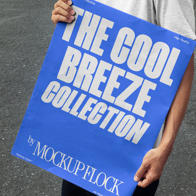 A person holds a poster that reads "THE COOL BREEZE COLLECTION BY MOCKUP FLOCK" in bold text, standing on black asphalt.