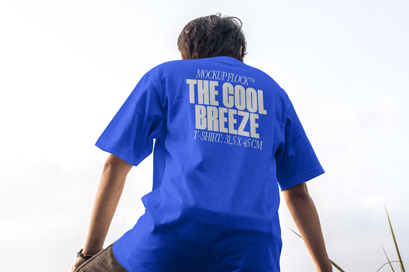 A person wearing a t-shirt that says "MOCKUP FLOCK THE COOL BREEZE T-SHIRT: 31,5X45CM" in bold text, on a blue sky background.