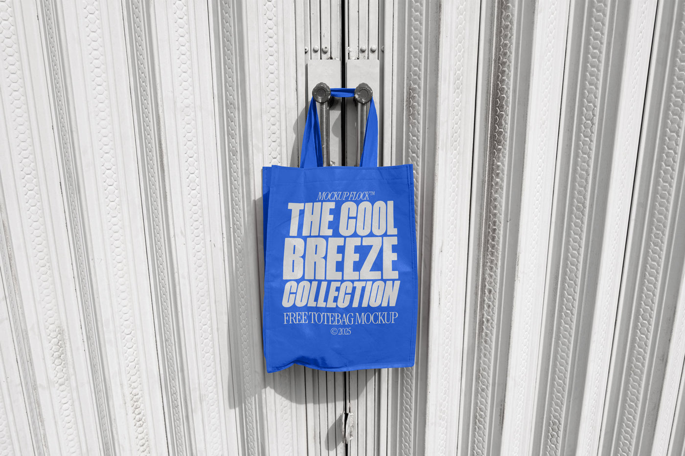 A blue tote bag with white text that reads "THE COOL BREEZE COLLECTION FREE TOTE BAG MOCKUP" hanging on a door handle.