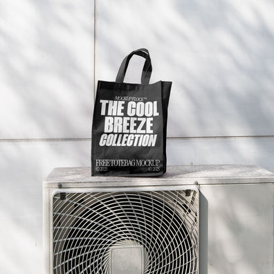 A black Poster with white text reading "MOCKUP FLOCK THE COOL BREEZE COLLECTION FREE TOTE BAG MOCKUP" is lying on outdoor air conditioner.