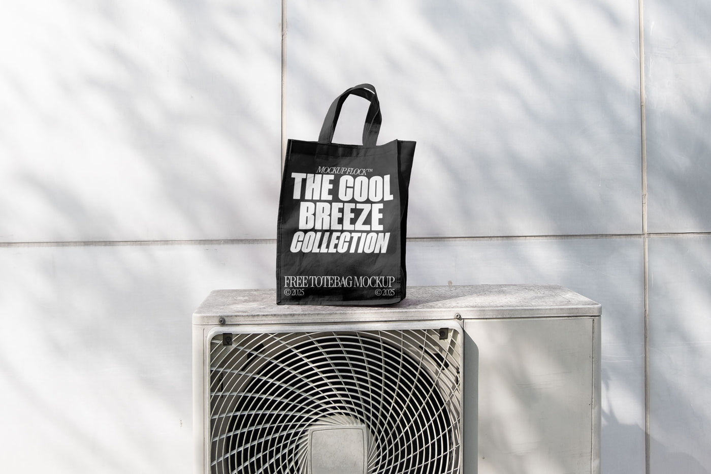 A black Poster with white text reading "MOCKUP FLOCK THE COOL BREEZE COLLECTION FREE TOTE BAG MOCKUP" is lying on outdoor air conditioner.