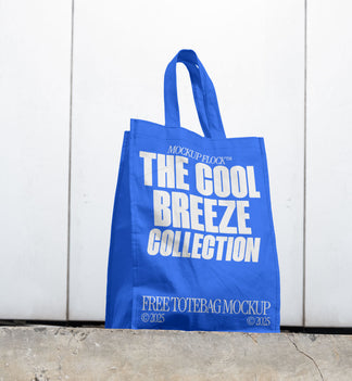 A blue poster with white text reading THE COOL BREEZE COLLECTION BY MOCKUP FLOCK is lying on the floor, on a white wall background.