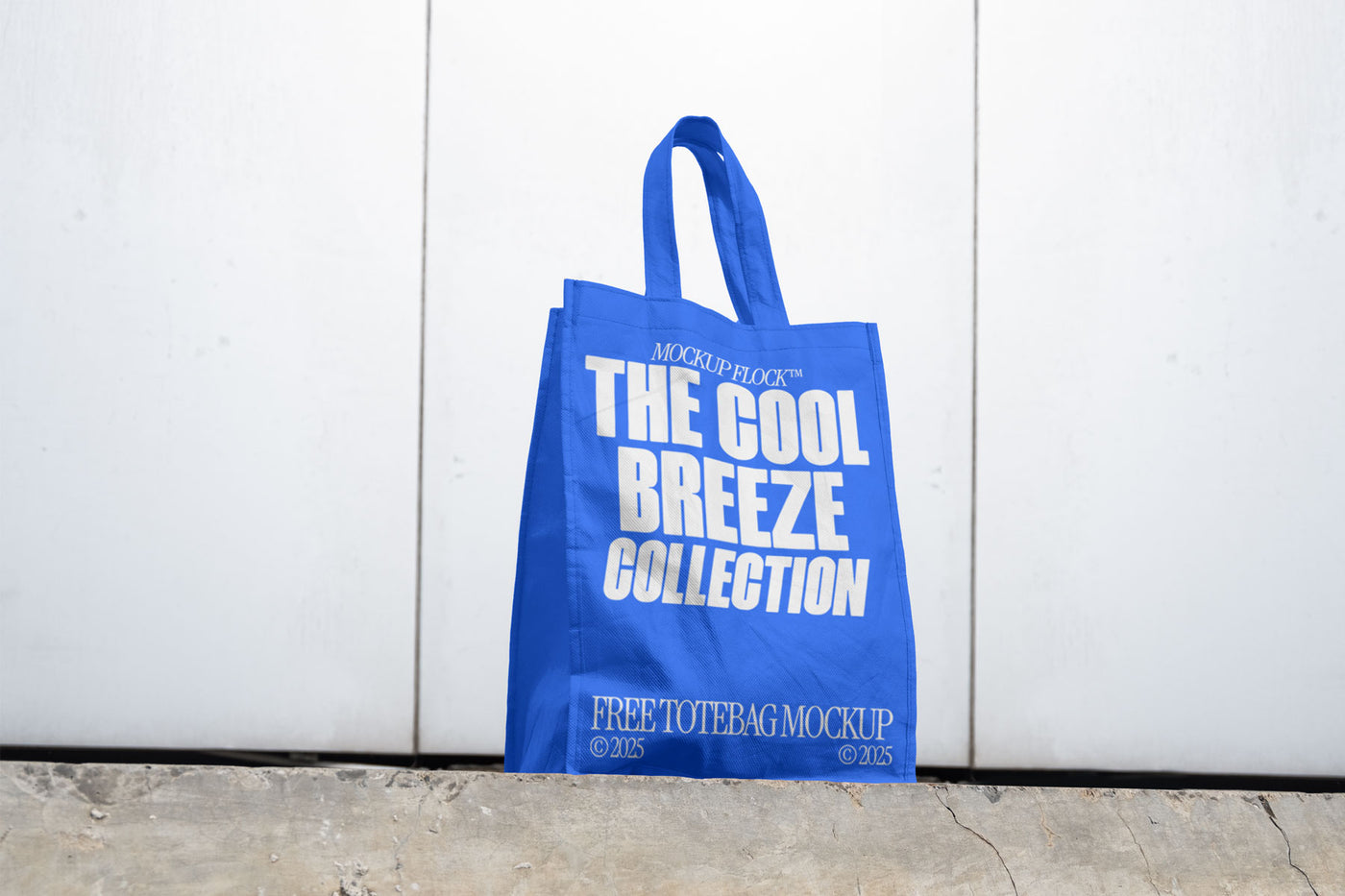 A blue poster with white text reading THE COOL BREEZE COLLECTION BY MOCKUP FLOCK is lying on the floor, on a white wall background.