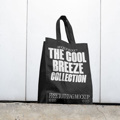 A black poster with white text reading THE COOL BREEZE COLLECTION BY MOCKUP FLOCK is lying on the floor, on a white wall background.