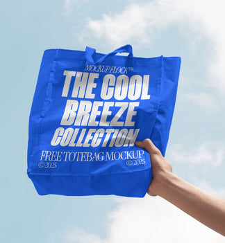 A person holds a tote bag that says "MOCKUP FLOCK THE COOL BREEZE COLLECTION FREE TOTE BAG MOCKUP" in bold text, on a blue sky background.