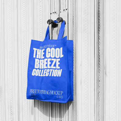 A blue tote bag with white text that reads "THE COOL BREEZE COLLECTION FREE TOTE BAG MOCKUP" hanging on a door handle.