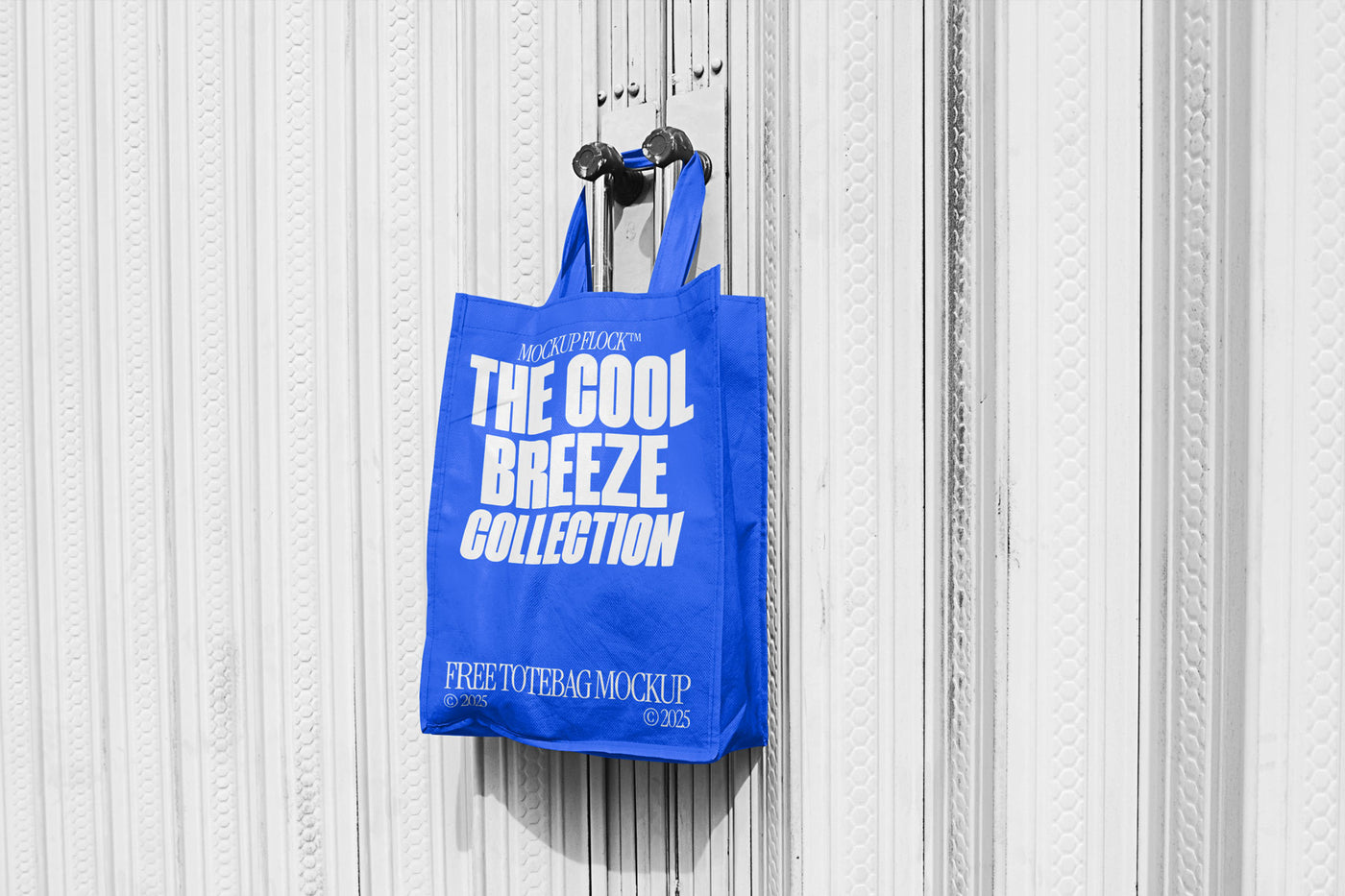 A blue tote bag with white text that reads "THE COOL BREEZE COLLECTION FREE TOTE BAG MOCKUP" hanging on a door handle.