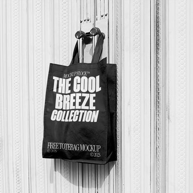 A black tote bag with white text that reads "THE COOL BREEZE COLLECTION FREE TOTE BAG MOCKUP" hanging on a door handle.