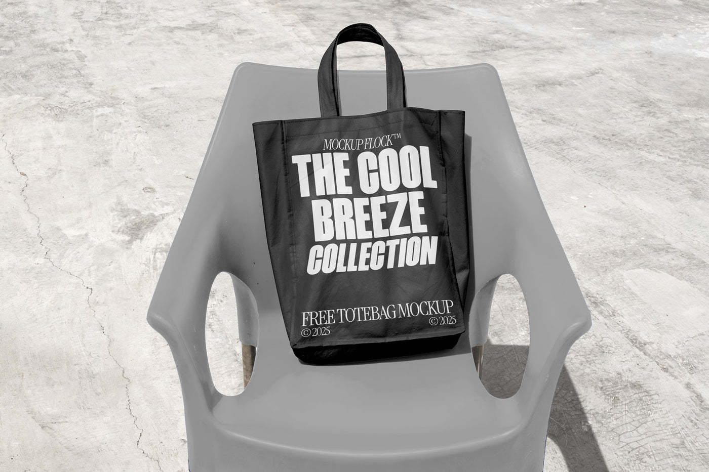 A black Poster with white text reading "THE COOL BREEZE COLLECTION FREE TOTE BAG MOCKUP" is lying on grey  chair.