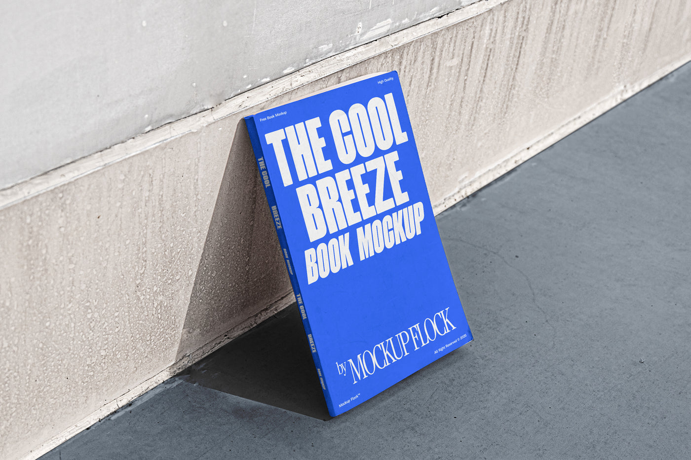 A blue book with white text reading THE COOL BREEZE BOOK MOCKUP BY MOCKUP FLOCK is lying on a clean floor, against the wall.
