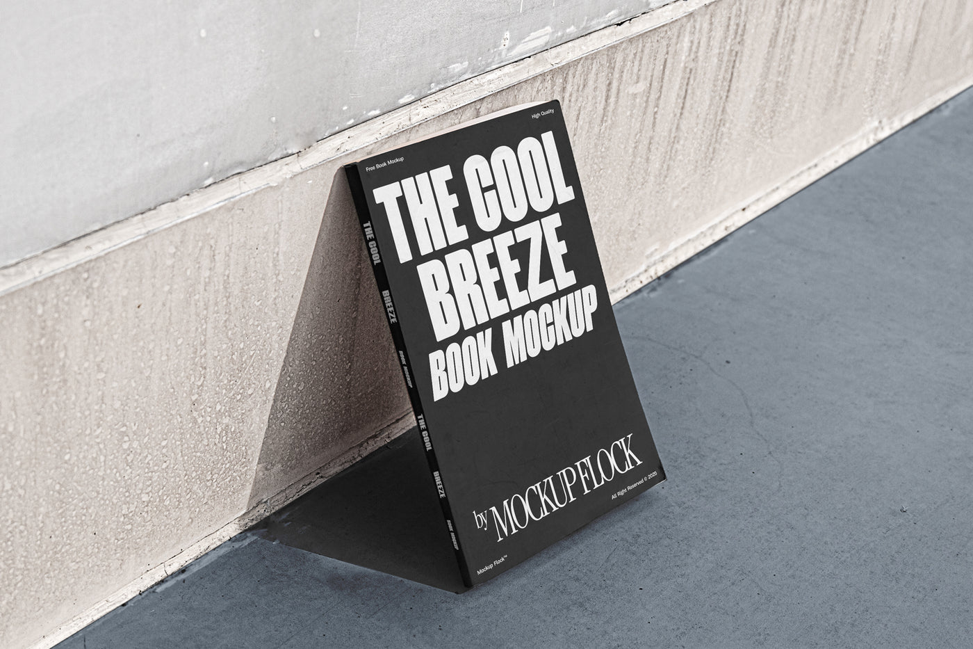A black book with white text reading THE COOL BREEZE BOOK MOCKUP BY MOCKUP FLOCK is lying on a clean floor, against the wall.