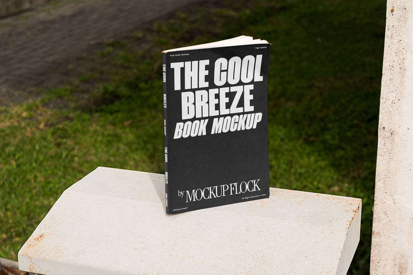 A black book with white text reading THE COOL BREEZE BOOK MOCKUP BY MOCKUP FLOCK is lying on a fence, displayed in a natural outdoor setting.