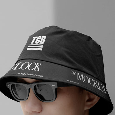 A person wearing a bucket hat and black glasses, written TCB and MOCKUP FLOCK.