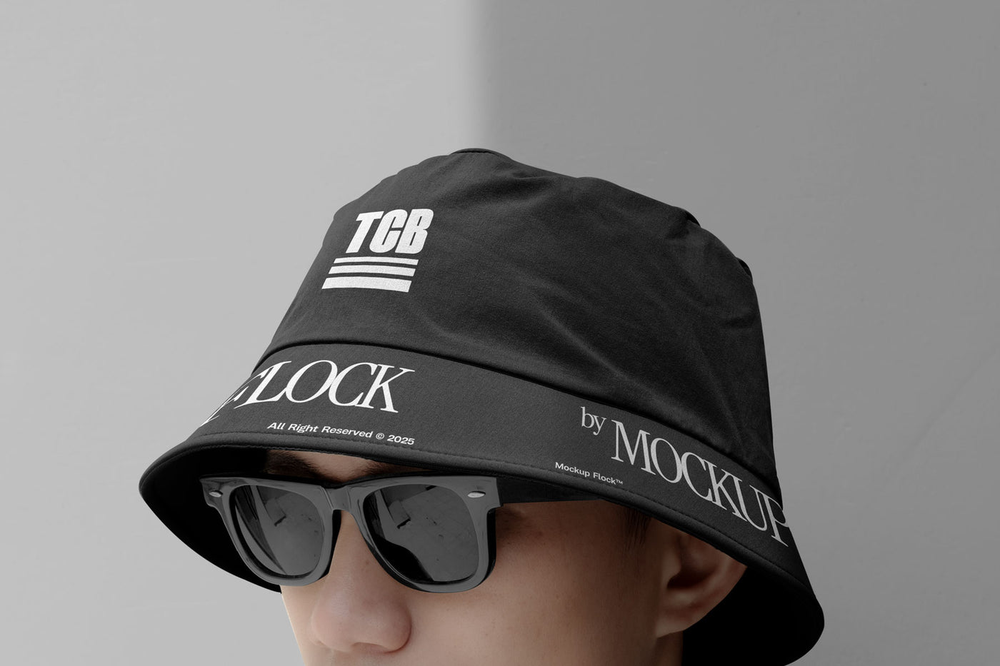 A person wearing a bucket hat and black glasses, written TCB and MOCKUP FLOCK.