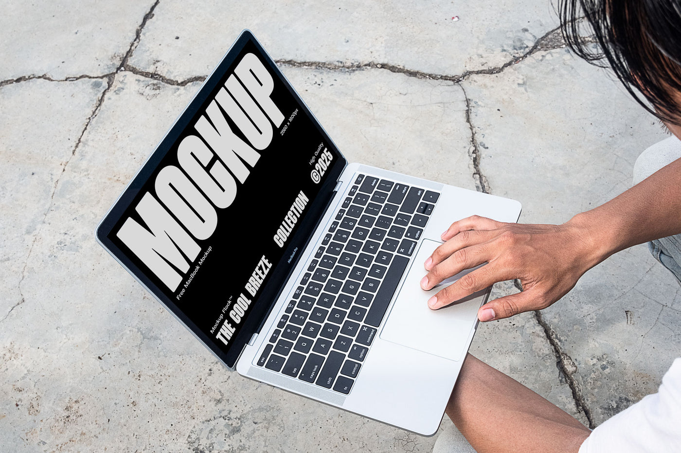 A person is holding an Macbook Device that says "MOCKUP THE COOL BREEZE COLLECTION @2025" in bold white text. Design by Mockup Flock
